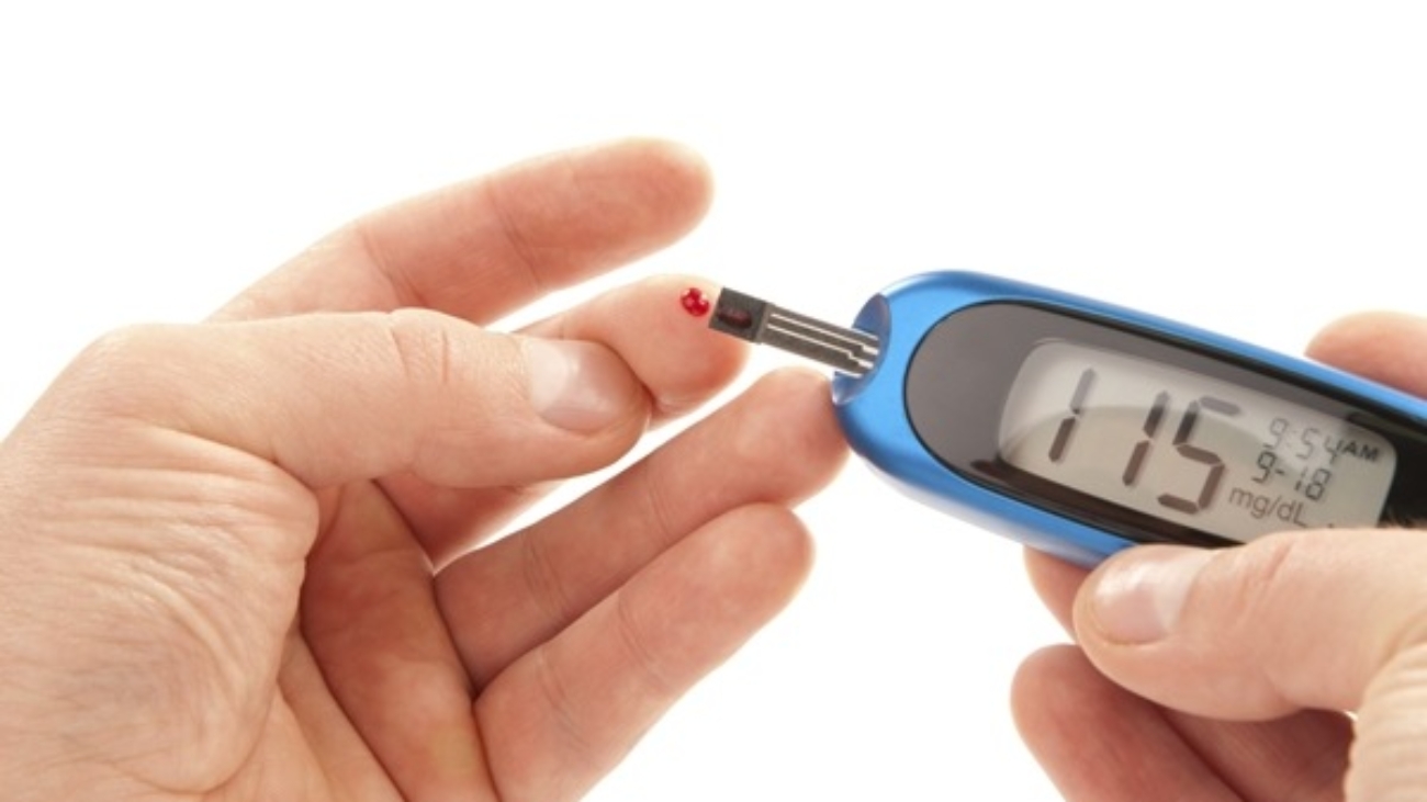 Diabetic patient doing glucose level blood test using ultra mini glucometer and small drop of blood from finger and test strips isolated on a white background. Device shows 115  mg/dL which is normal