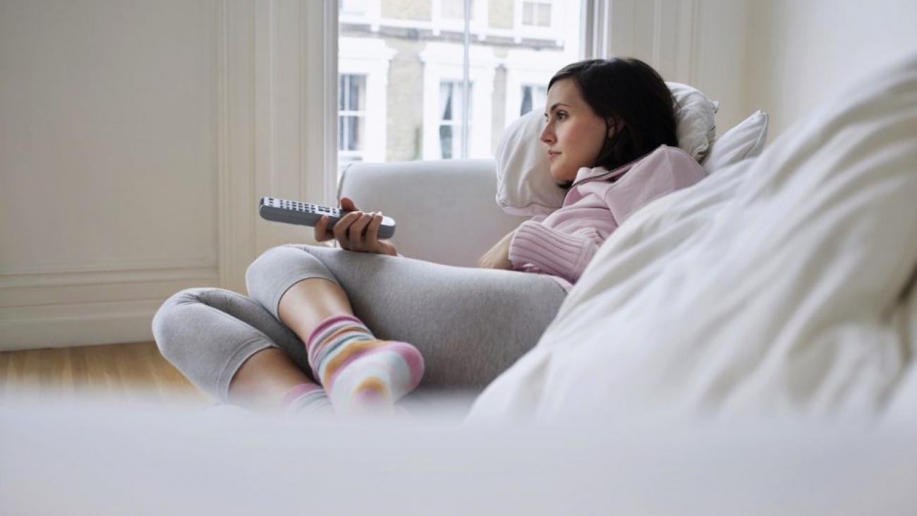 Young woman lying on couch and watching television